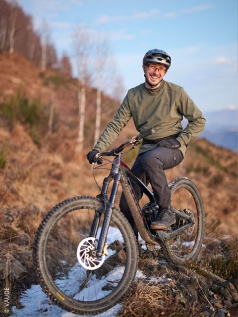 Una persona con casco e giacca verde sorride mentre posa con una mountain bike s