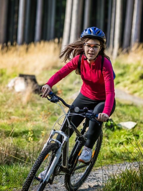 Una donna in maglietta rossa e con il casco va in mountain bike su un sentiero n