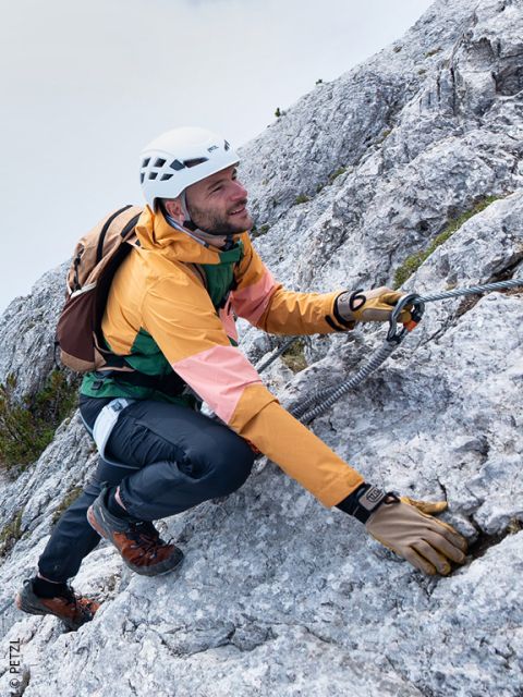 Un uomo con attrezzatura da arrampicata sale su un ripido pendio roccioso, tenen