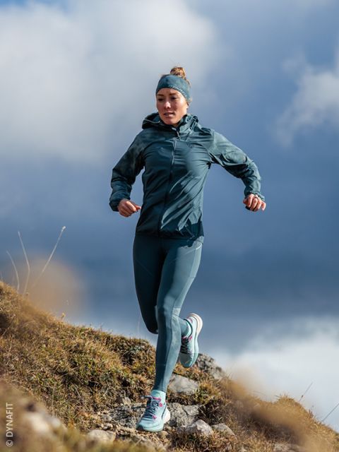 Una donna in abbigliamento sportivo color turchese corre in discesa su un sentie