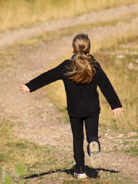 Una ragazza con i capelli lunghi e un vestito nero corre felicemente con le brac